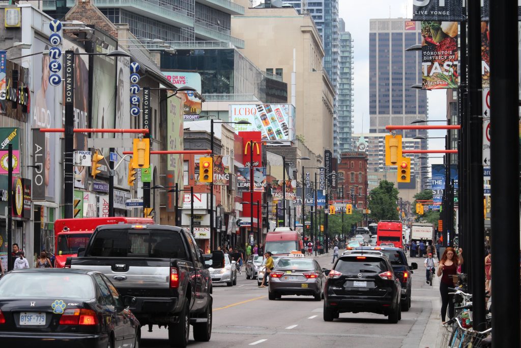 Busy Toronto street with cars, pedestrians, and storefronts including McDonald's and The Bay. Takeoff-Moving Toronto